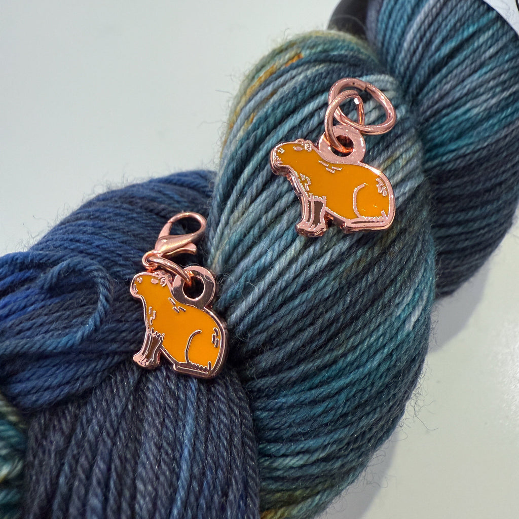 Two capybara charms on a skein of blue yarn.