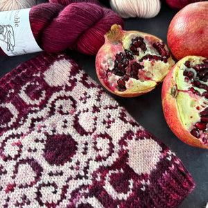 Knitted cowl with a pomegranate and filigree motif with pomegranates and yarn on a dark surface
