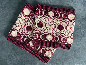 Knitted cowls with burgundy and light pink pomegranate and filigree pattern on a dark surface