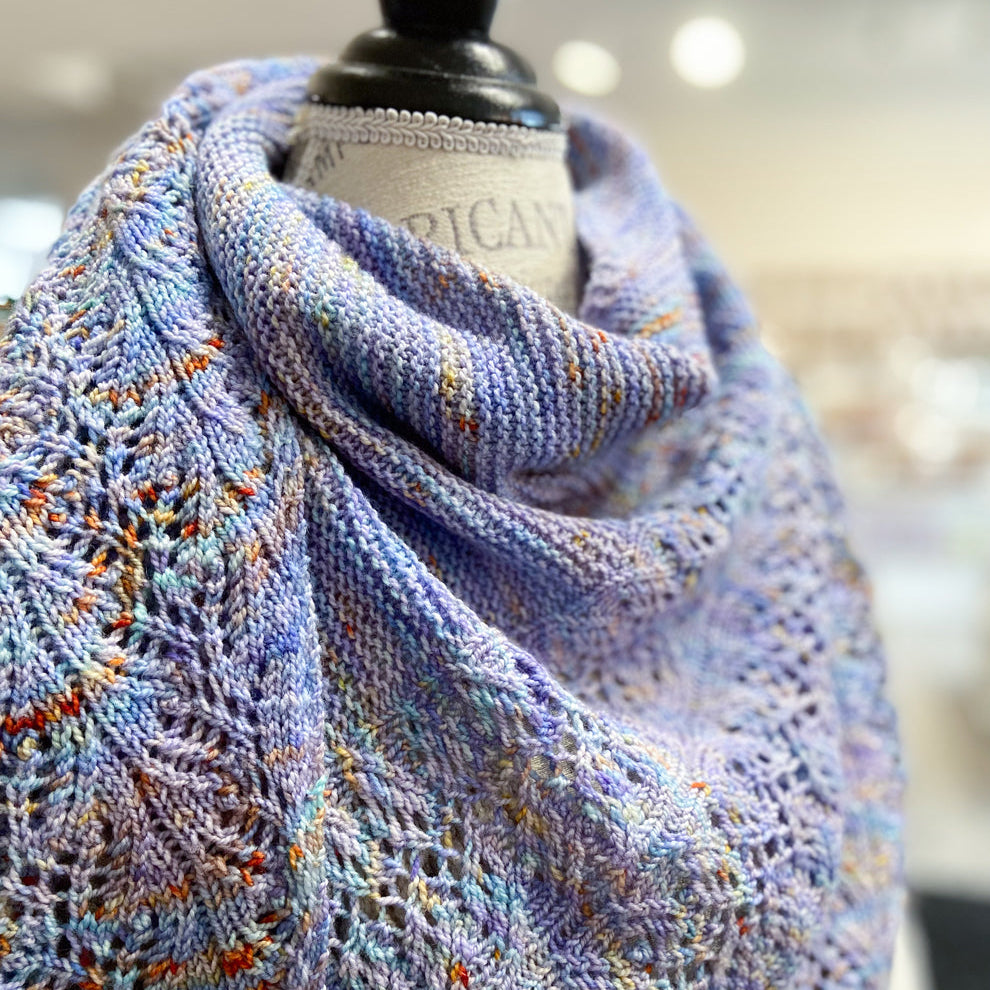 Knitted light blue shawl with orange speckles on a mannequin with a blurred background