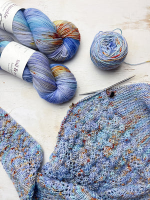 Blue with orange and gold speckles yarn skeins with a knitted fabric on a light wooden surface