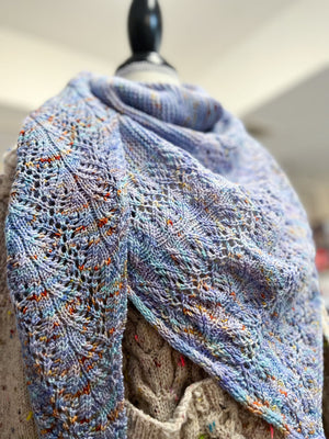 Knitted shawl draped over a mannequin with a blurred indoor background