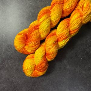 Skeins of bright yellow and orange tweed sock yarn with colorful neon slubs, displayed on a dark textured surface.