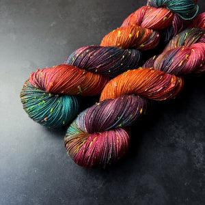 Skeins of aqua, orange, pink, and purple tweed sock yarn with colorful neon slubs, displayed on a dark textured surface.