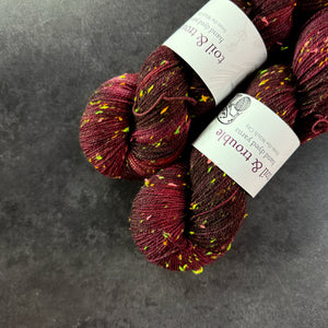 Skeins of red and burgundy tweed sock yarn with colorful neon slubs, displayed on a dark textured surface.