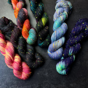 Array of colorful skeins of yarn with neon tweed slubs on a dark background