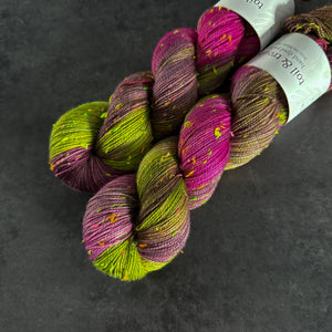 Skeins of magenta and bright green tweed sock yarn with colorful neon slubs, displayed on a dark textured surface.