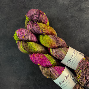 Skeins of magenta and bright green tweed sock yarn with colorful neon slubs, displayed on a dark textured surface.