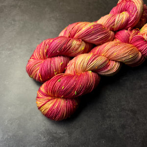 Skeins of pink and yellow variegated tweed sock yarn with colorful neon slubs, displayed on a dark textured surface.