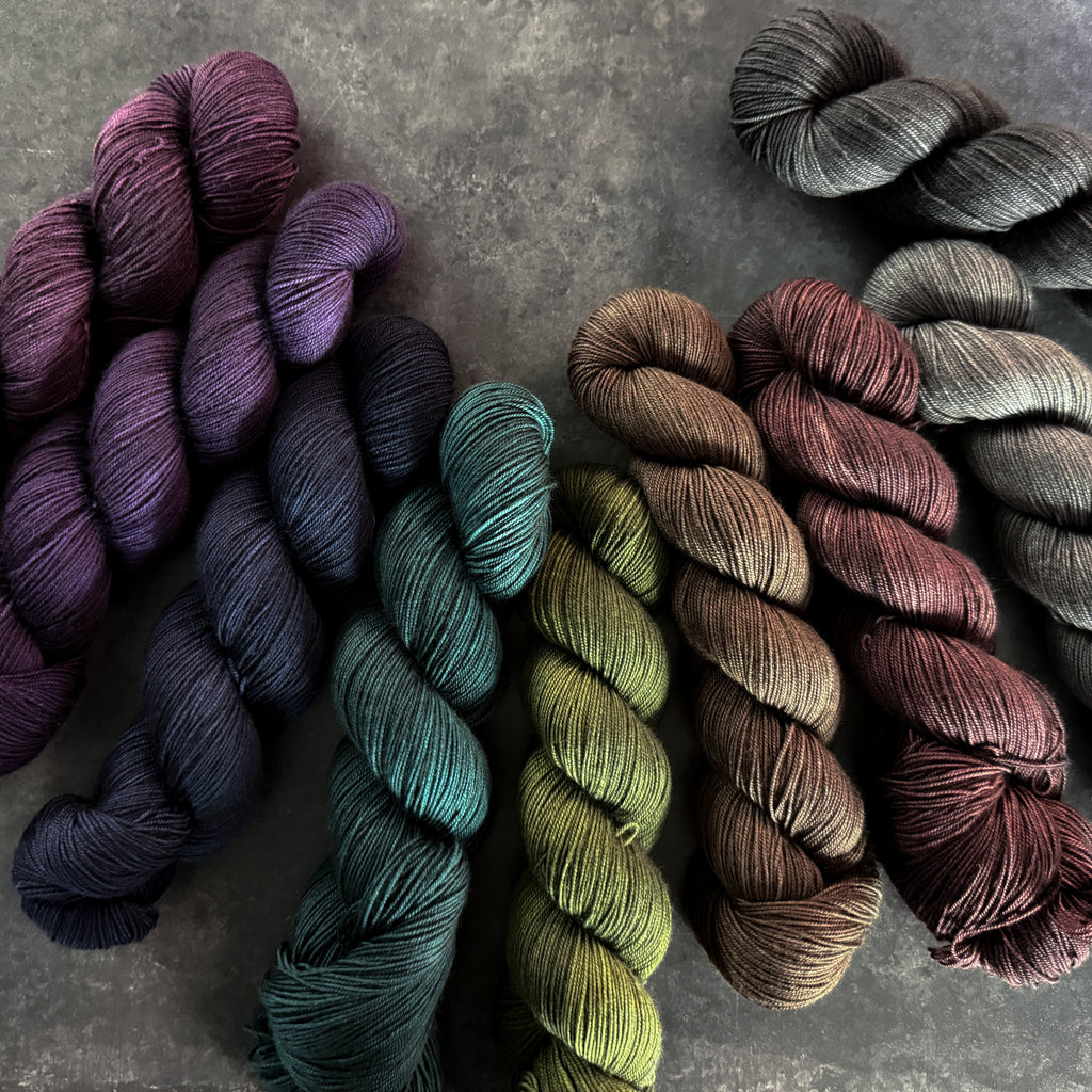 Collection of skeins of yarn in various moody colors on a dark textured surface