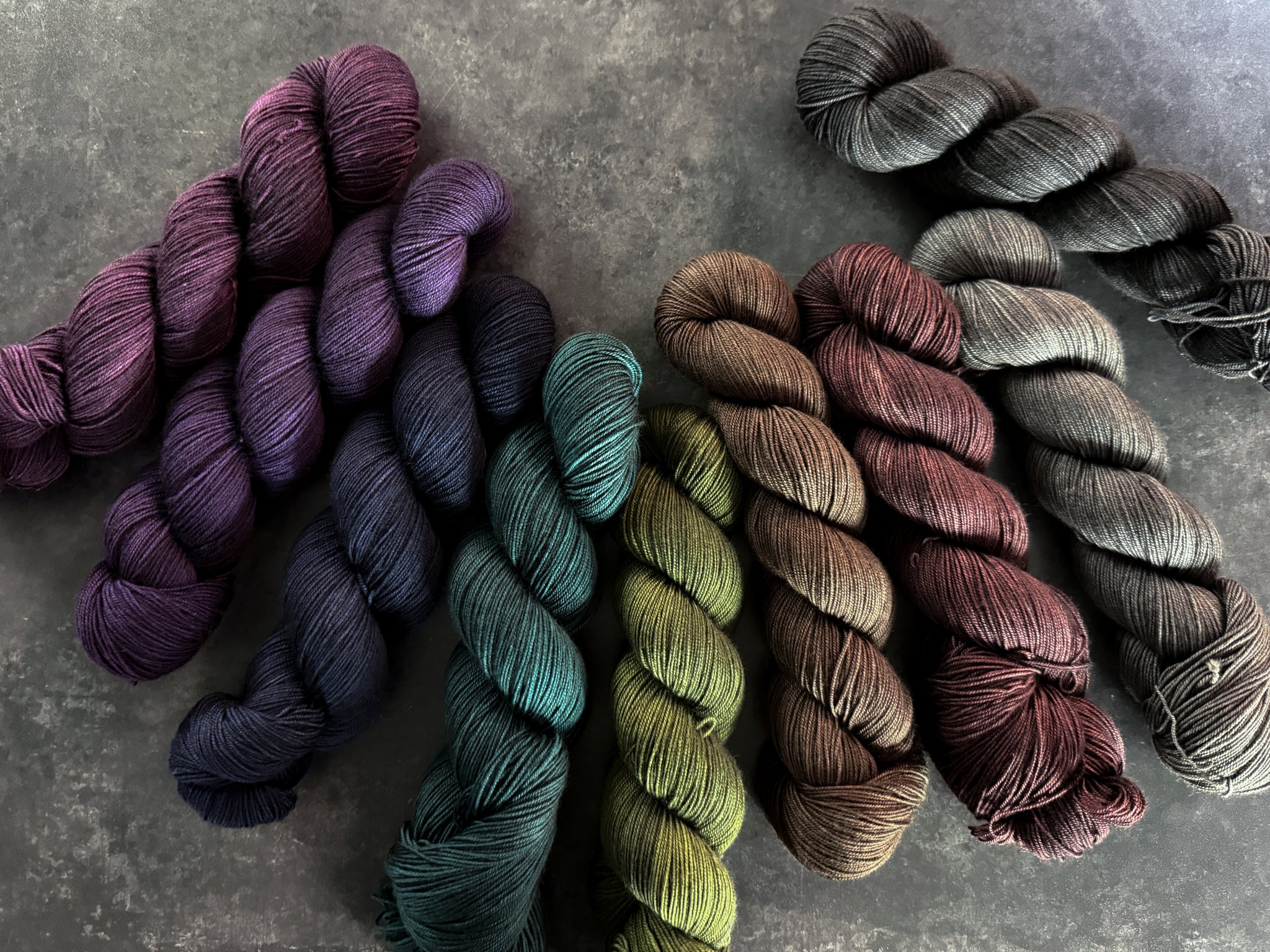 Collection of skeins of yarn in various moody colors on a dark textured surface