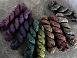 Collection of skeins of yarn in various moody colors on a dark textured surface