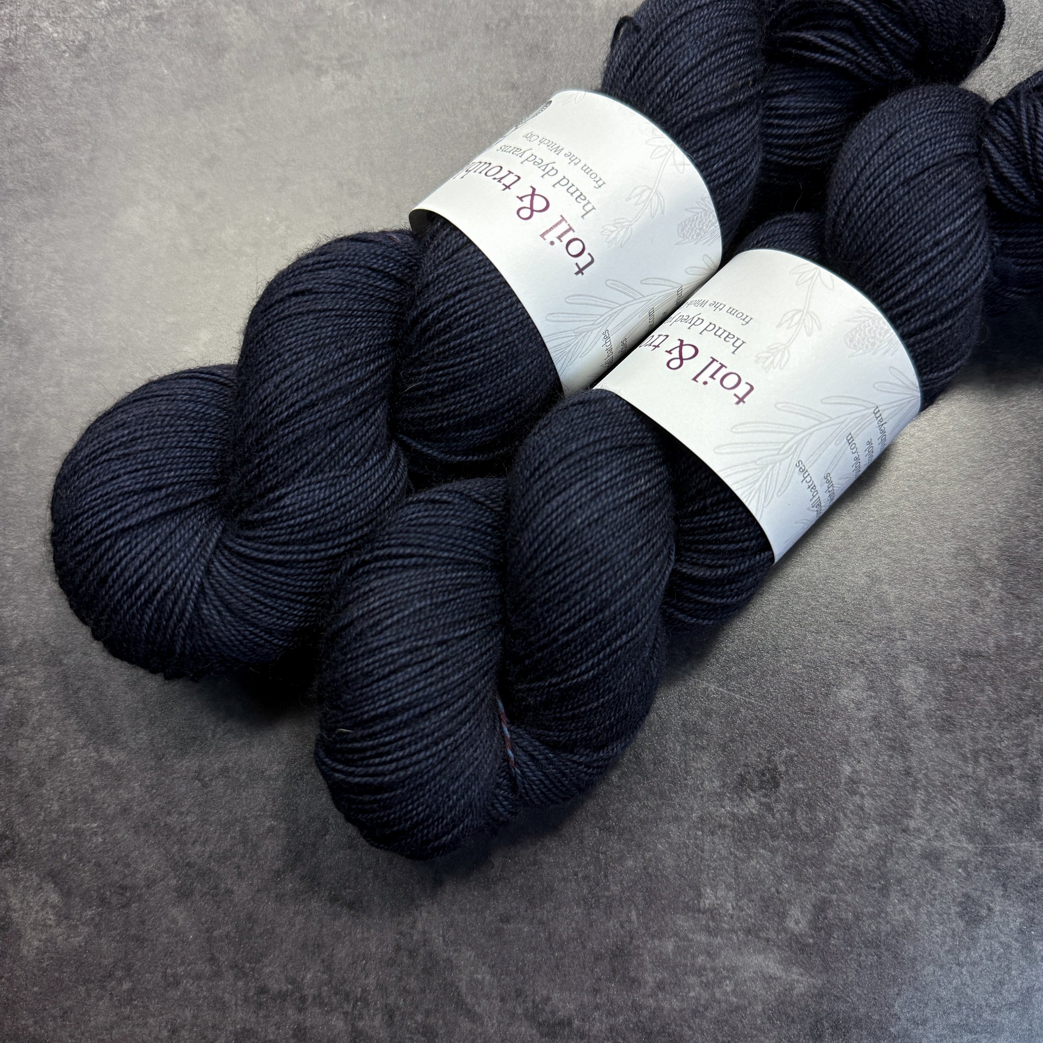 Two skeins of dark blue yarn with labels on a gray surface