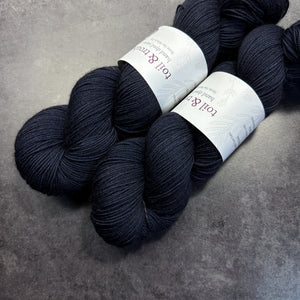Two skeins of dark blue yarn with labels on a gray surface