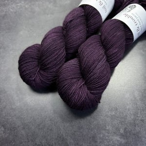 Two skeins of dark purple yarn on a gray surface with visible brand labels.