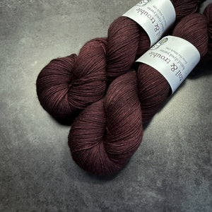 Two skeins of dark reddish brown yarn with labels on a gray surface