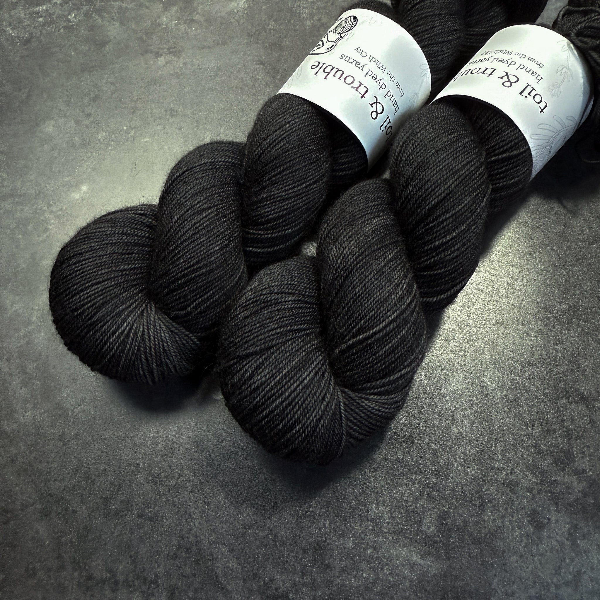 Two skeins of black yarn with labels on a gray surface
