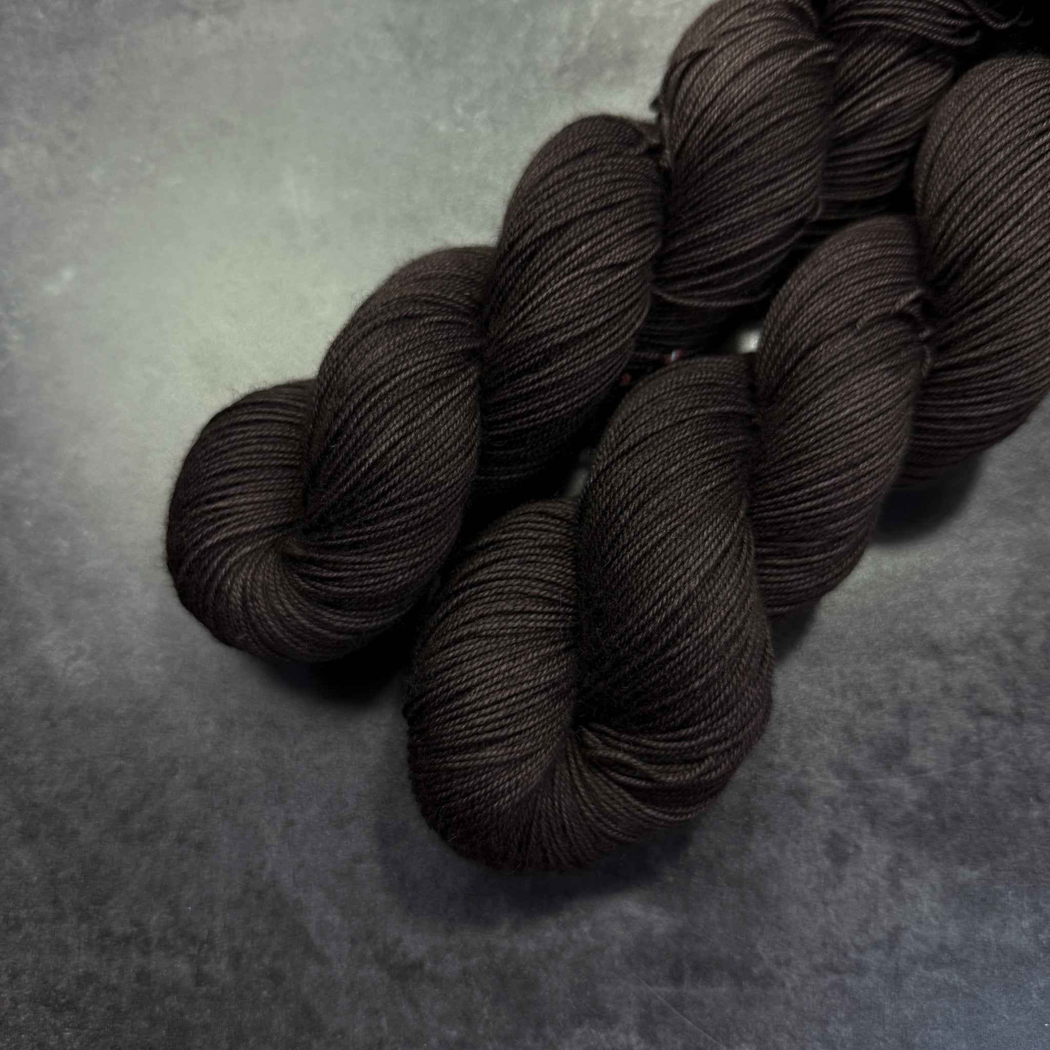Two skeins of dark brown yarn on a gray surface