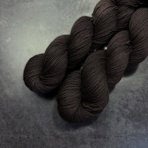 Two skeins of dark brown yarn on a gray surface