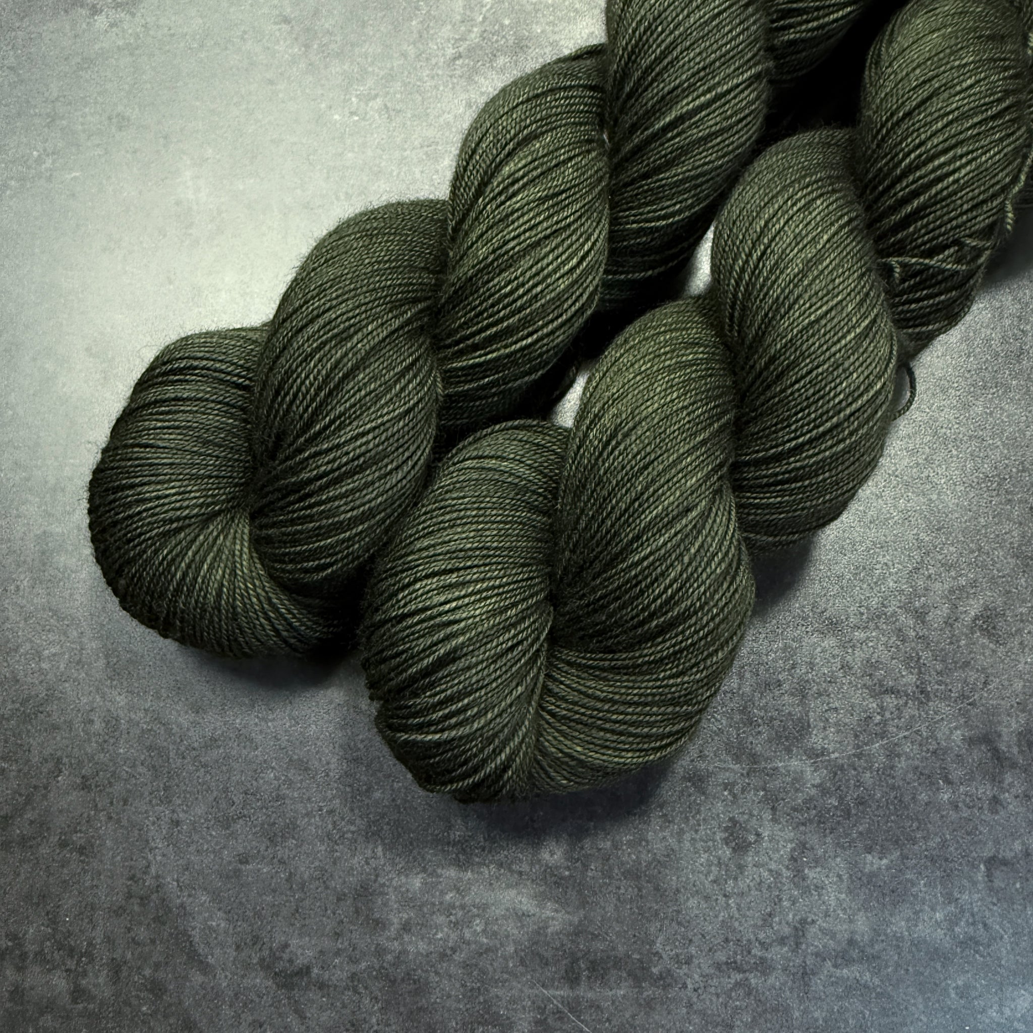 Two skeins of dark green yarn on a textured gray surface