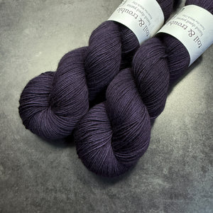 Two skeins of dark purple yarn with labels on a gray surface