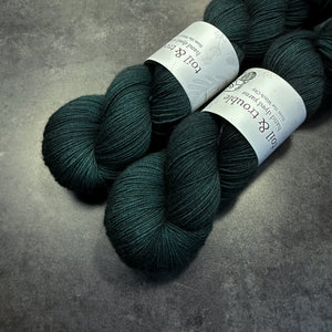 Two skeins of dark teal yarn with labels on a gray surface