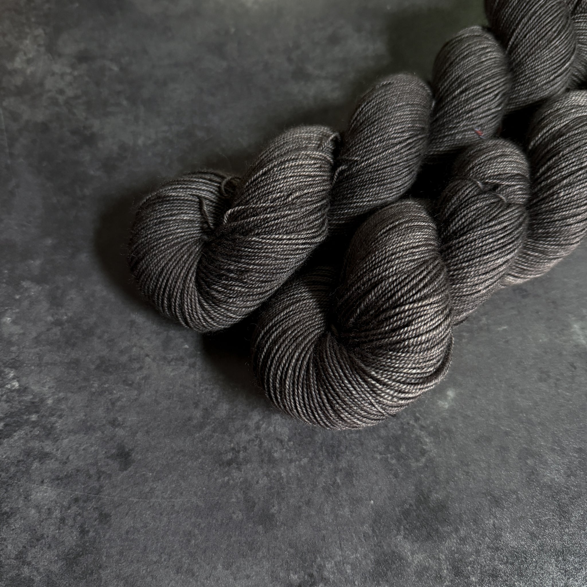 Two gray skeins of yarn on a dark gray textured surface