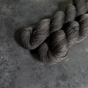 Two gray skeins of yarn on a dark gray textured surface